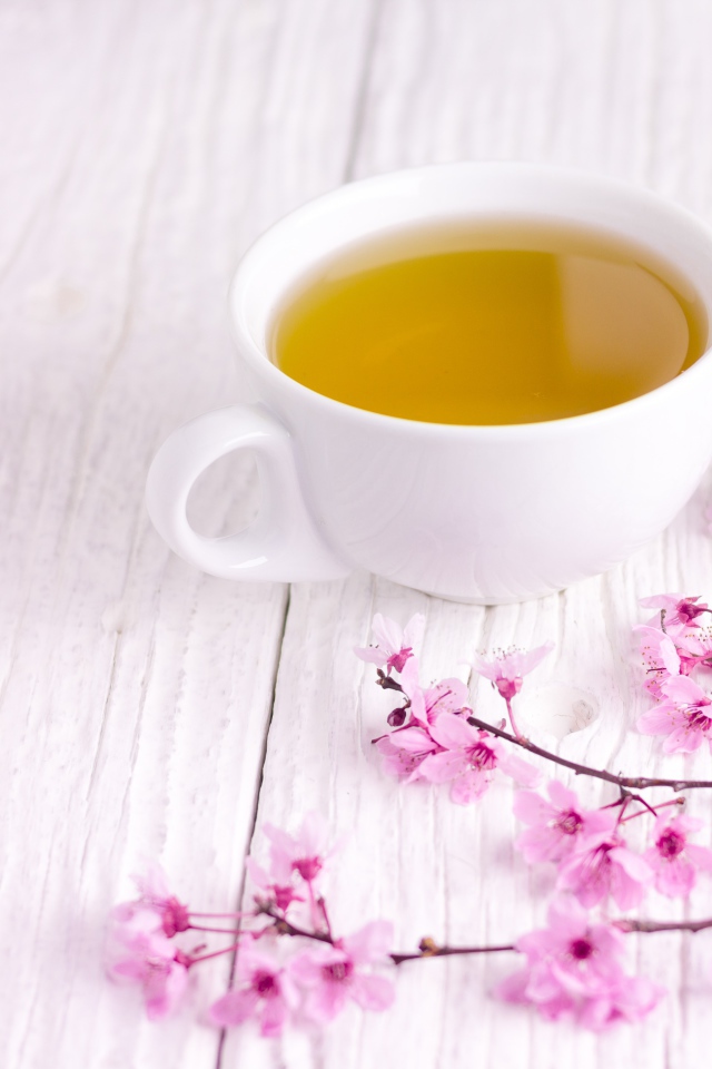 Белая чашка зеленого чая на столе с розовыми цветами