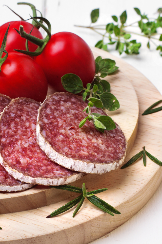 Вкусная колбаса на разделочной доске с помидорами и зеленью 