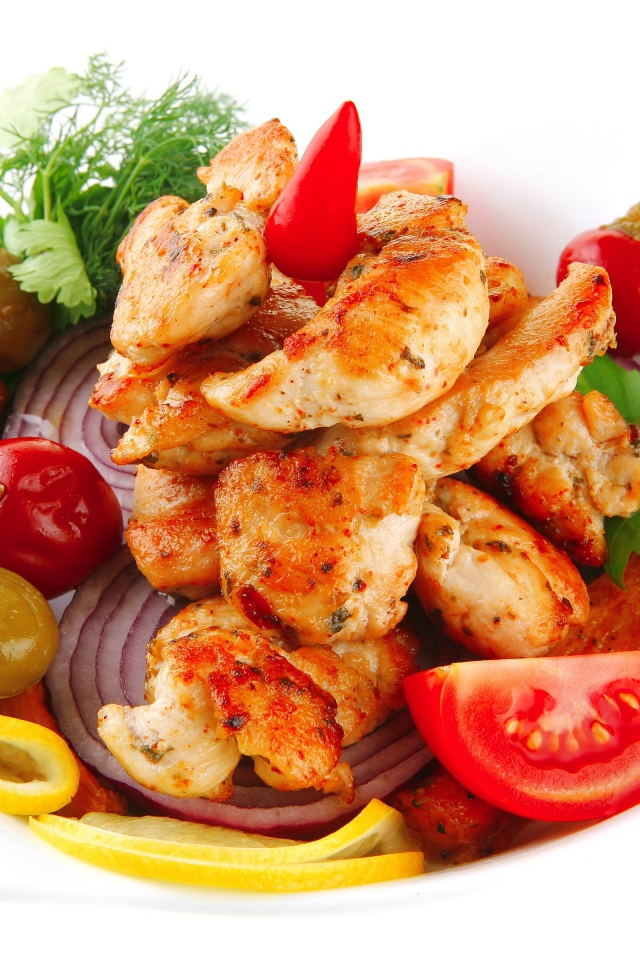 Жареные кусочки курицы на тарелке с овощами и зеленью 