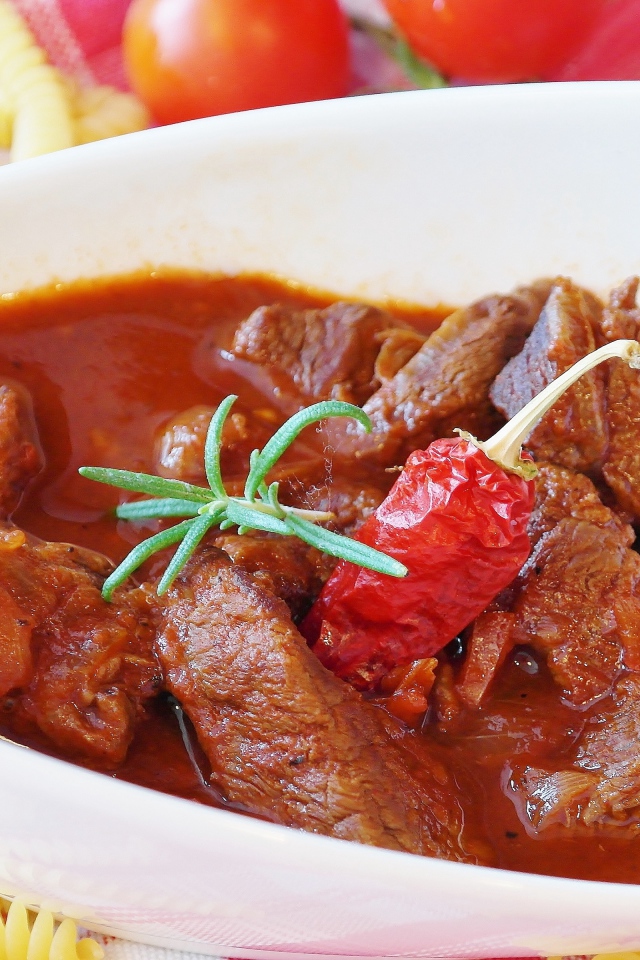 Мясной гуляш в белой тарелке с острым перцем