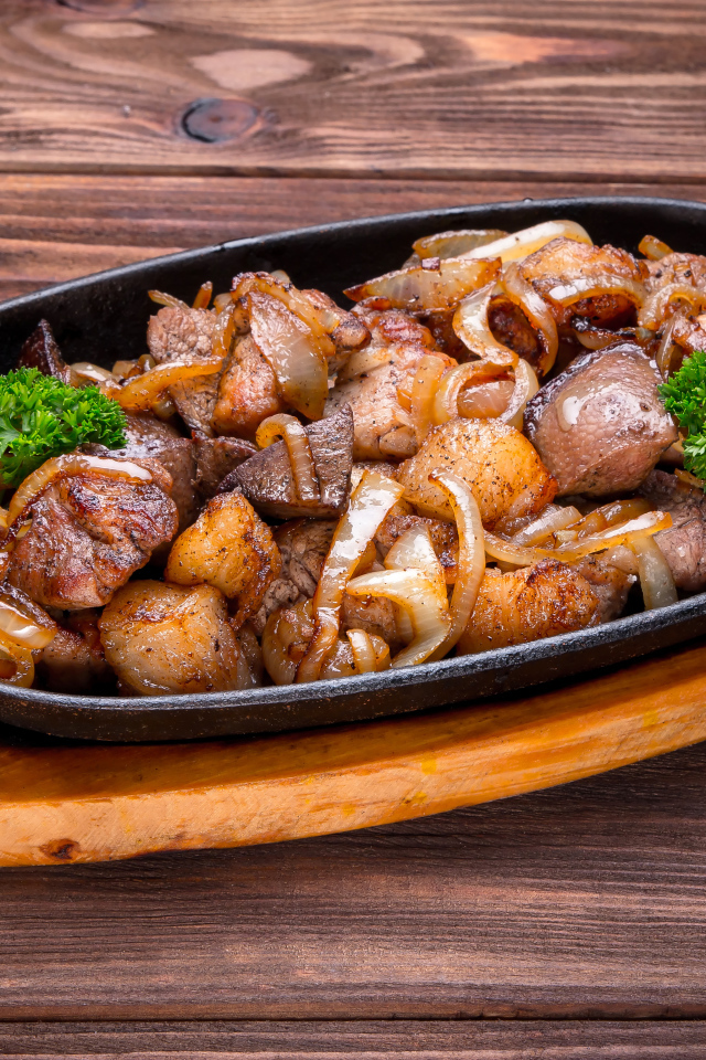 Кусочки шашлыка с луком и петрушкой в сковороде