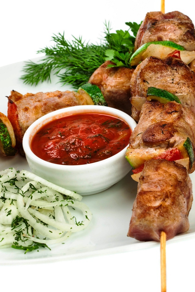 Шашлык на белой тарелке с соусом, зеленью и луком