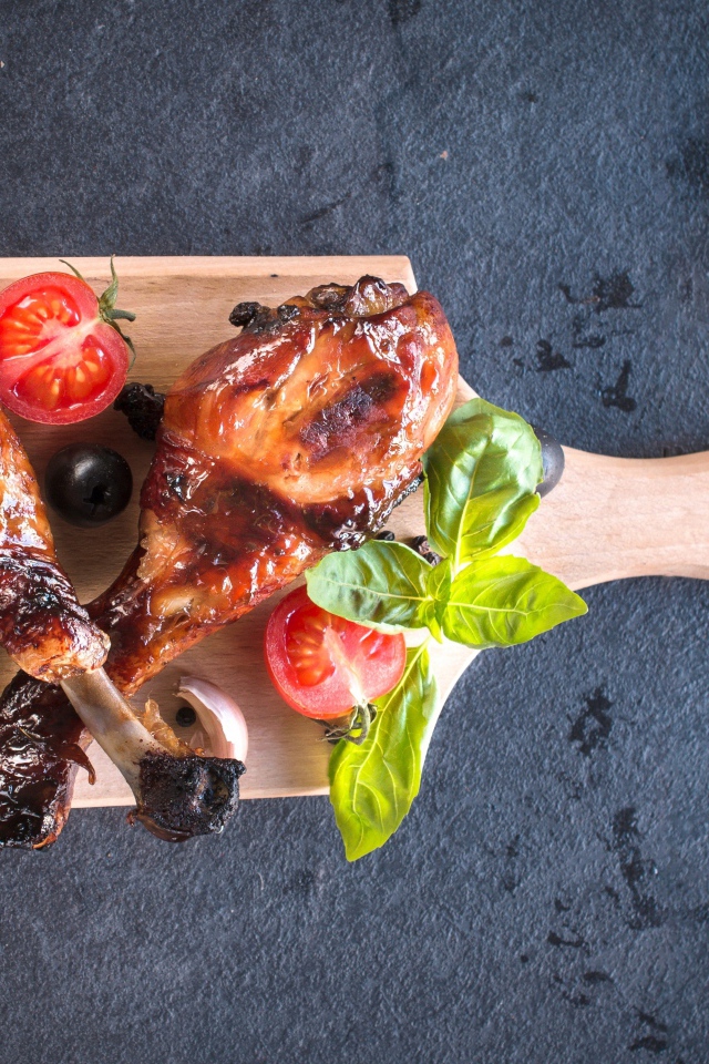 Две зажаренных куриных ножки с овощами на разделочной доске