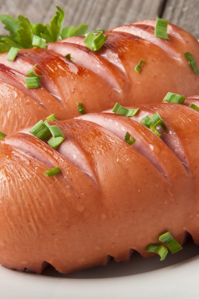 Два жареные сардельки на большой белой тарелке с зеленью 