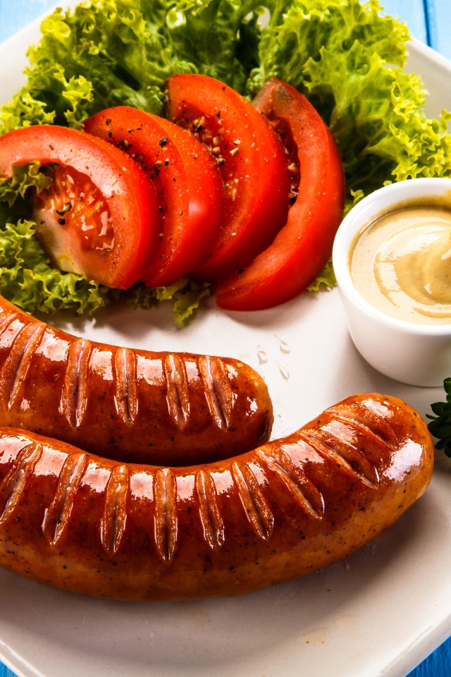 Две сосиски гриль на тарелке с овощами и горчицей