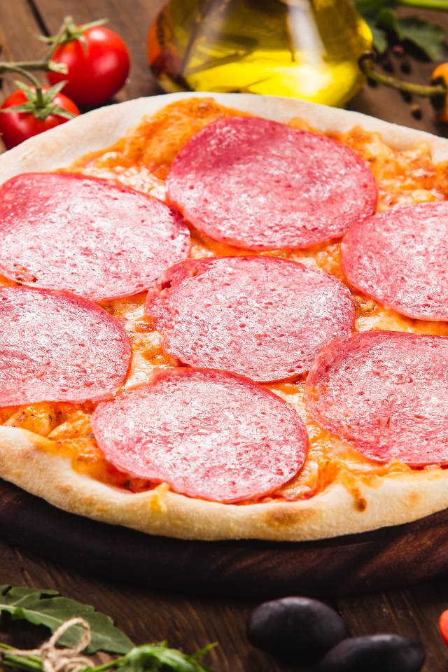 Пицца с салями на столе с овощами 