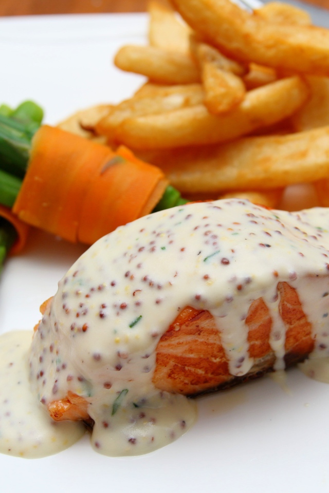 Кусок жареной красной рыбы с соусом на тарелке с картофелем фри 