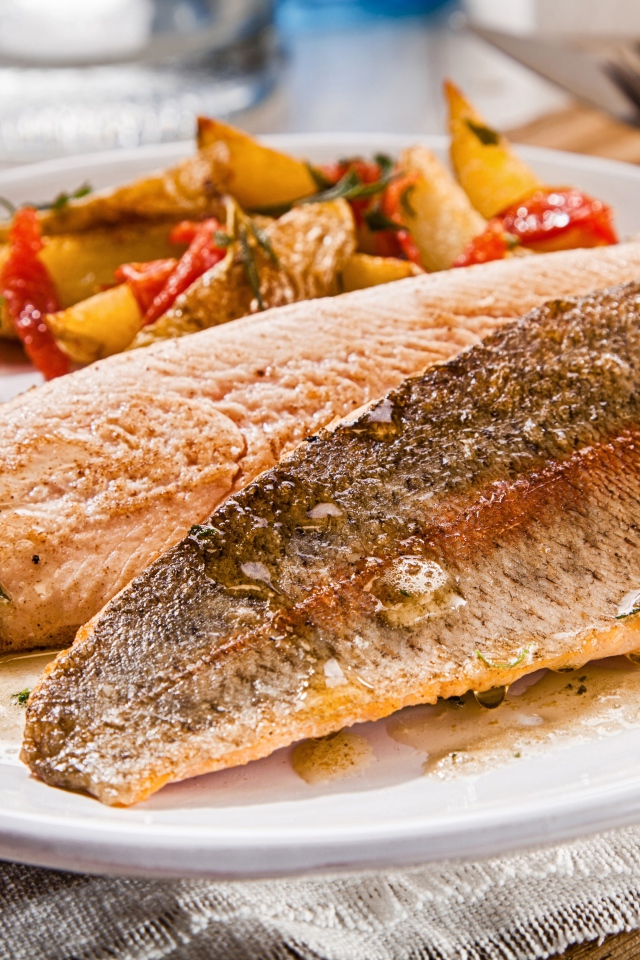 Baked fish with tomatoes and vegetables on a white plate