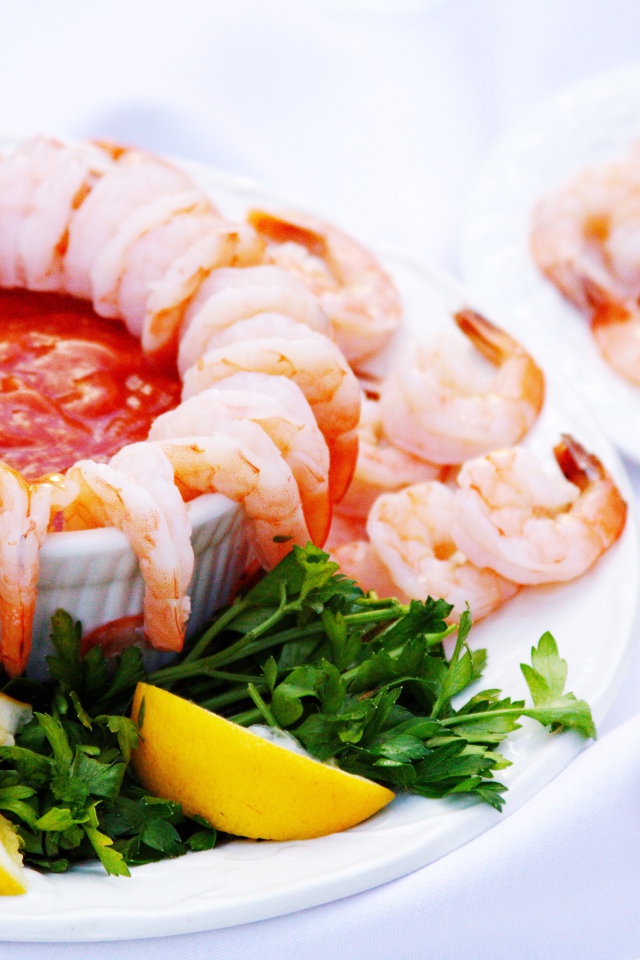 Вареные креветки с соусом на тарелке с лимоном и зеленью петрушки 