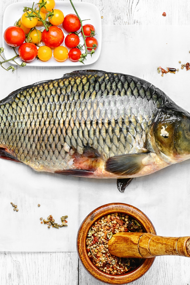 Свежий карась на столе со специями и помидорами