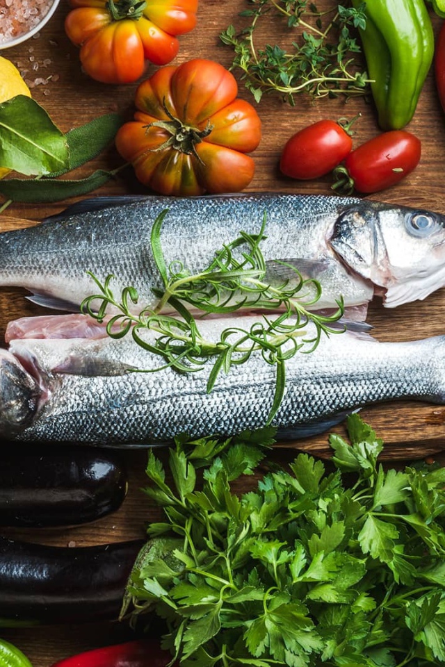 Свежая рыба на столе с овощами и зеленью 