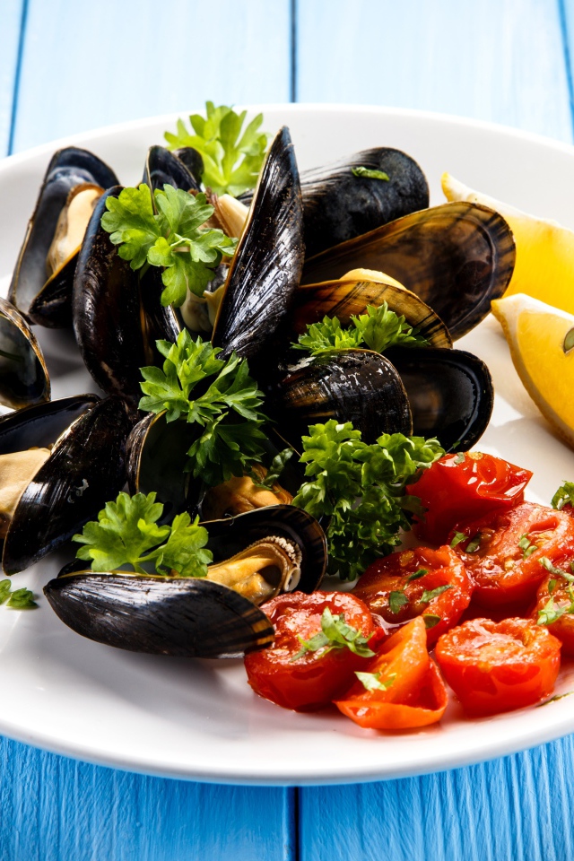 Мидии с томатами, кусочками лимона и зеленью петрушки на белой тарелке