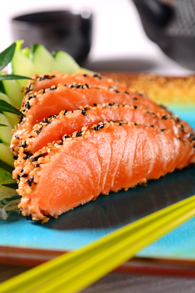 Красная рыба с листьями салата и свежими огурцами на тарелке с палочками