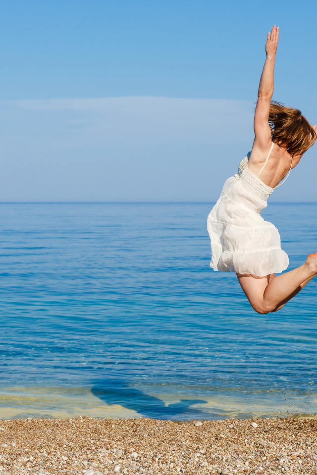 Молодая девушка в белом платье делаем прыжок на песке у моря