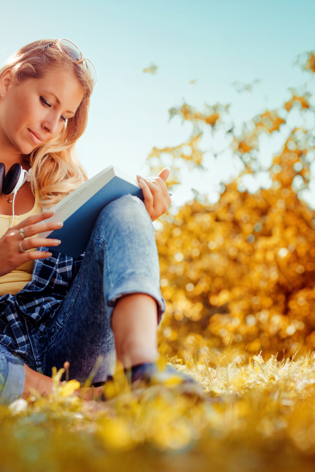 Молодая девушка читает книгу на желтой траве осенью