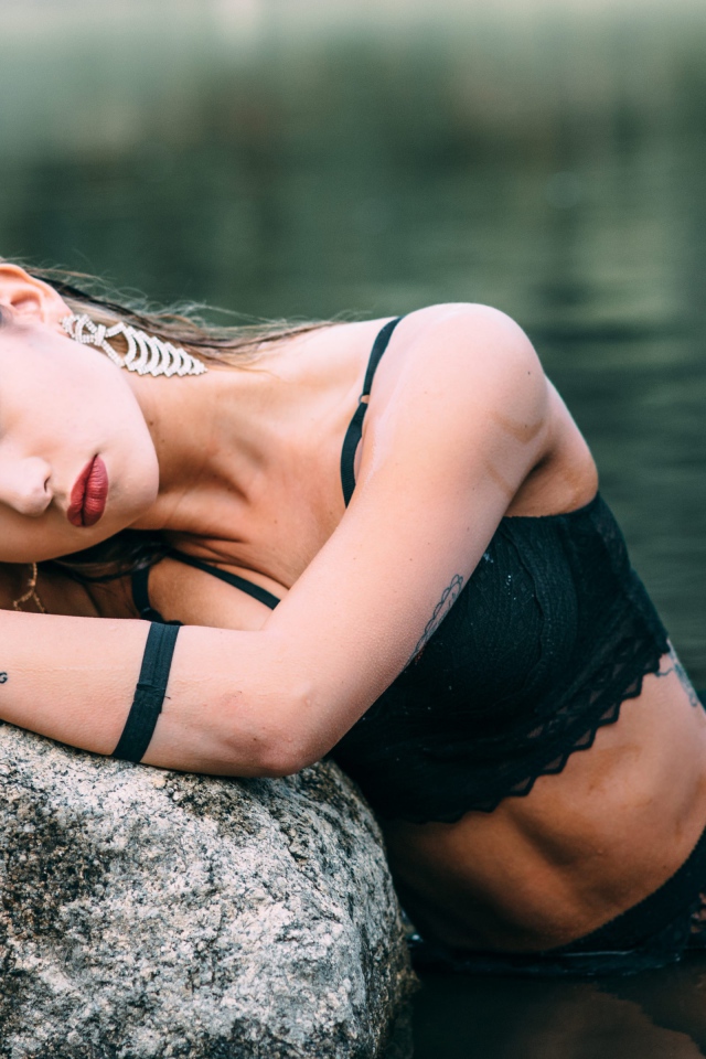 Молодая девушка с татуировками сидит у камня в воде