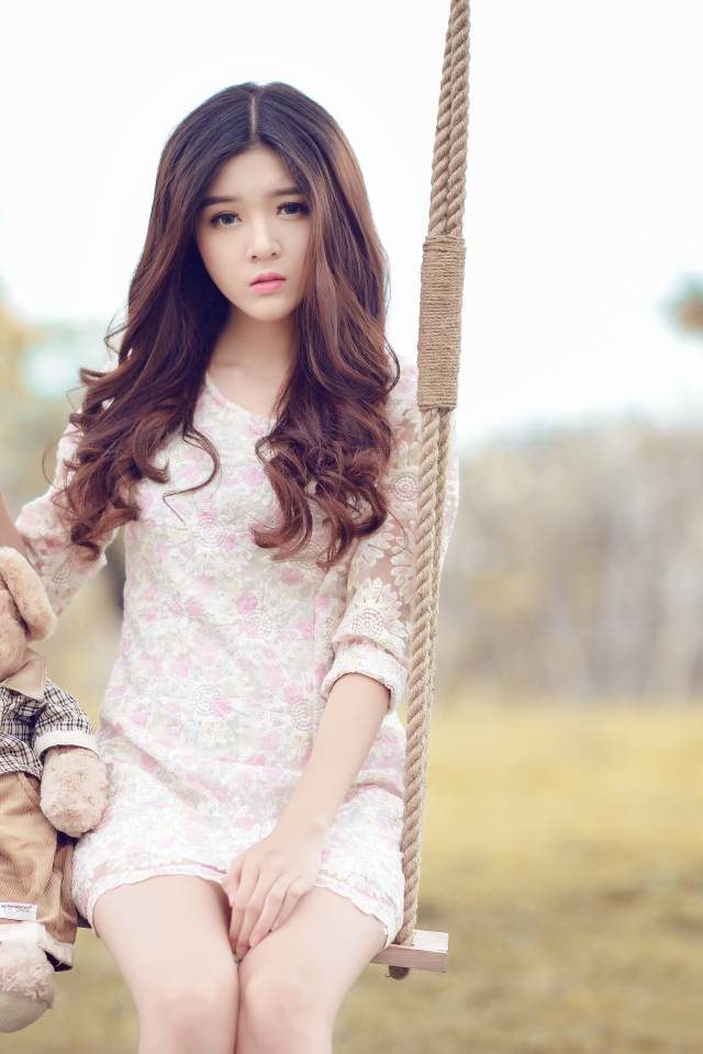 Девочка азиатка сидит на качели с плюшевым мишкой