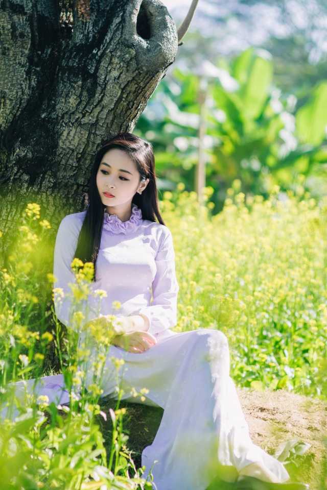 Красивая девушка азиатка сидит в белом платье под деревом