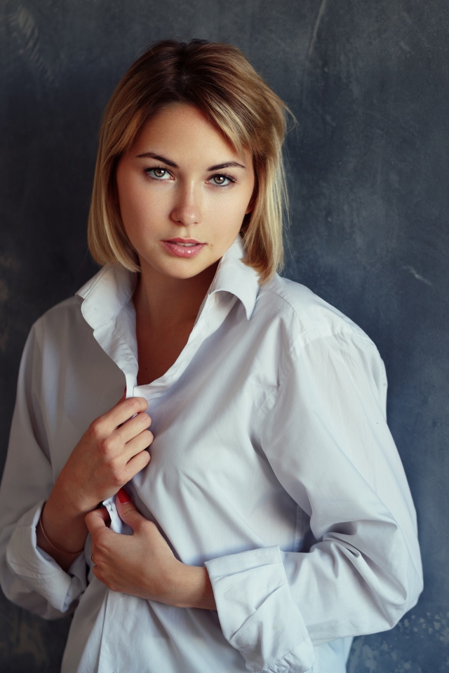 Красивая девушка блондинка в белой рубашке у стены 