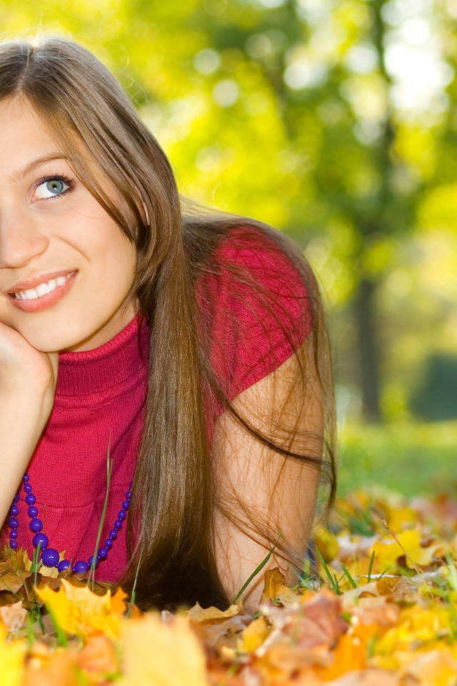 Красивая голубоглазая шатенка лежит на траве с желтыми листьями