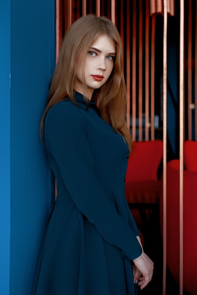 Красивая голубоглазая девушка стоит в пальто у стены