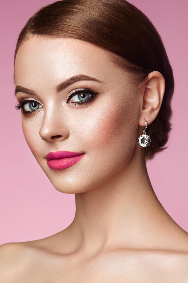 Красивая голубоглазая девушка с красивыми серьгами на розовом фоне