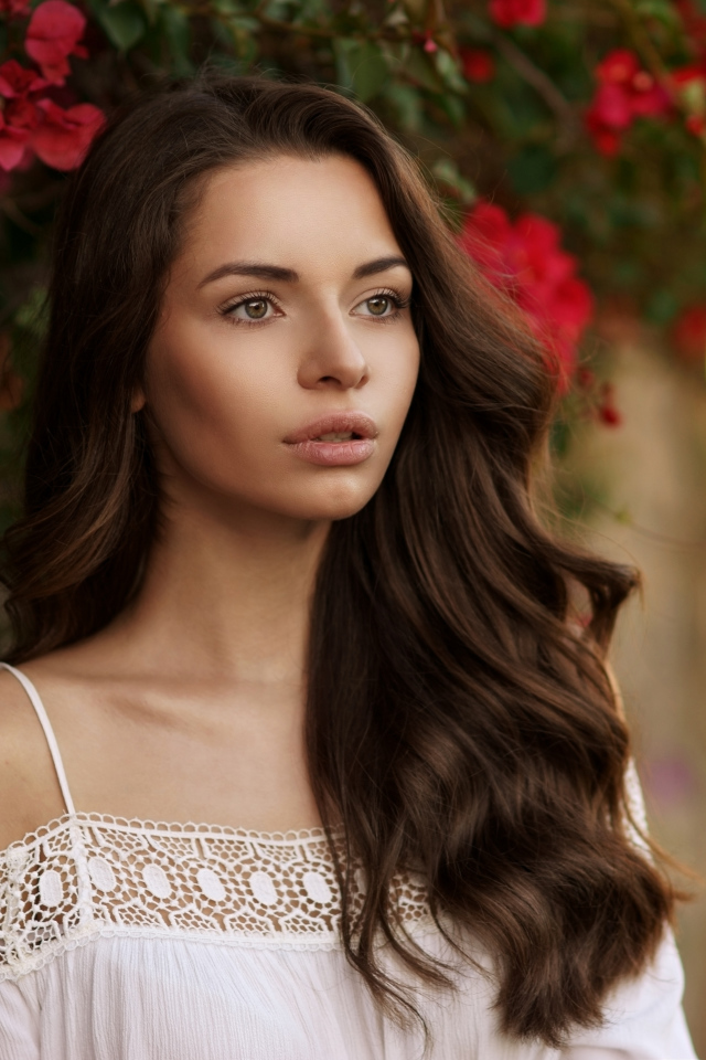 Красивая шатенка у стены на фоне красных цветов