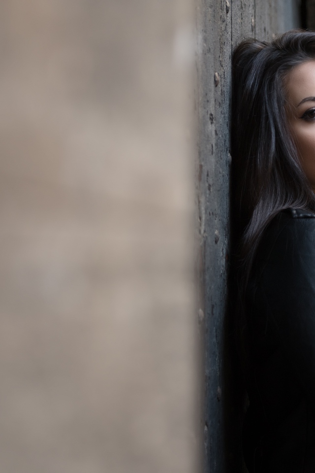 Красивая  брюнетка в кожаной куртке стоит у стены