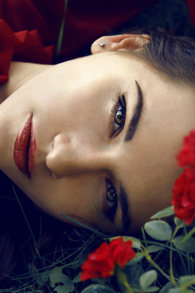 Красивая брюнетка лежит на траве с красными розами