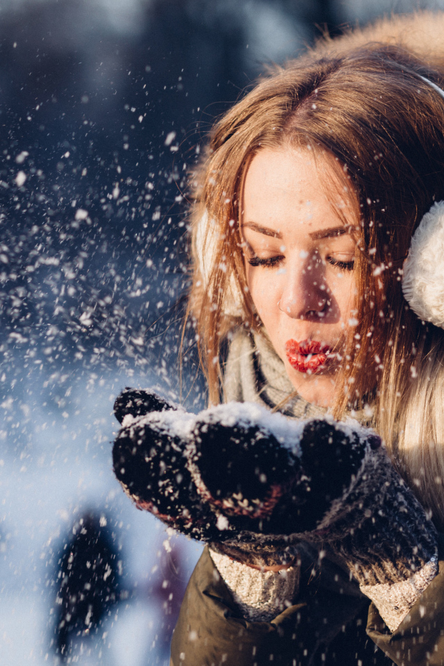 Красивая девушка сдувает снег с ладоней зимой