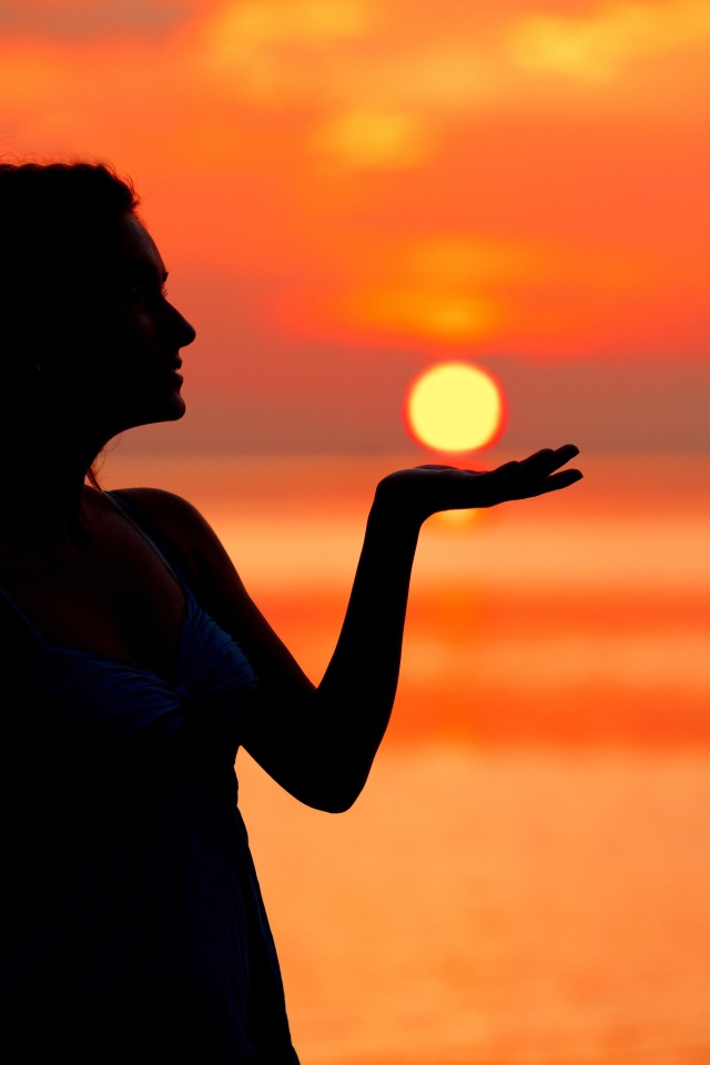 Красивая девушка держит солнце в ладони на закате