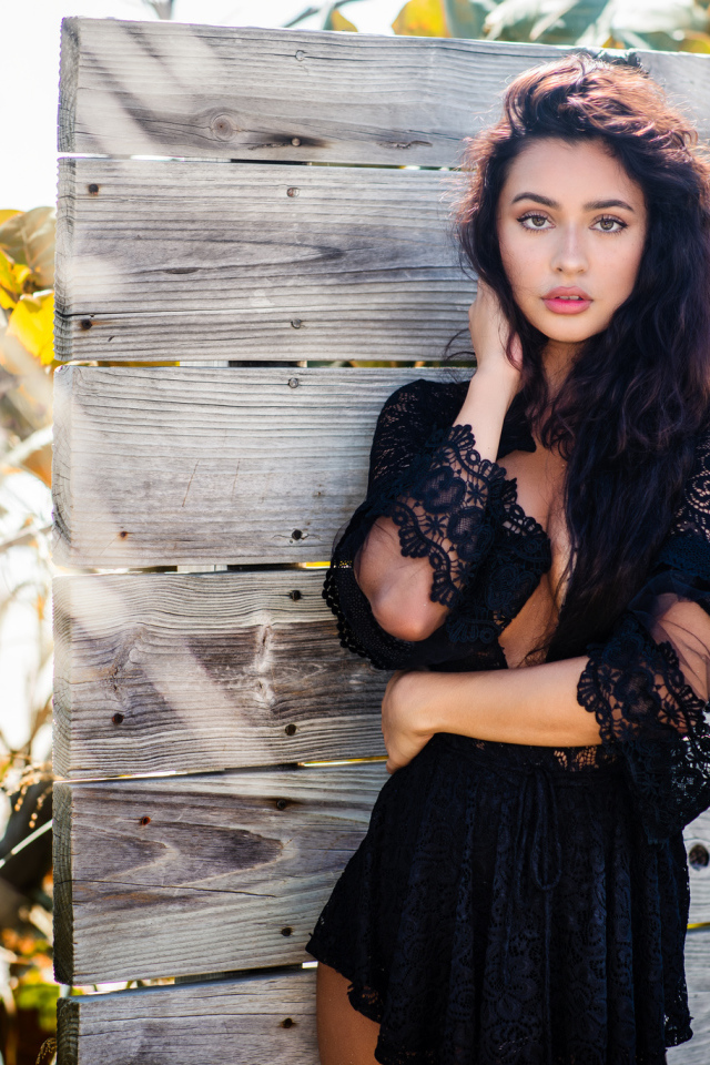 Красивая девушка в черном платье у стены 