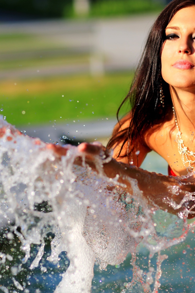 Красивая девушка в красном платье делает брызги на воде