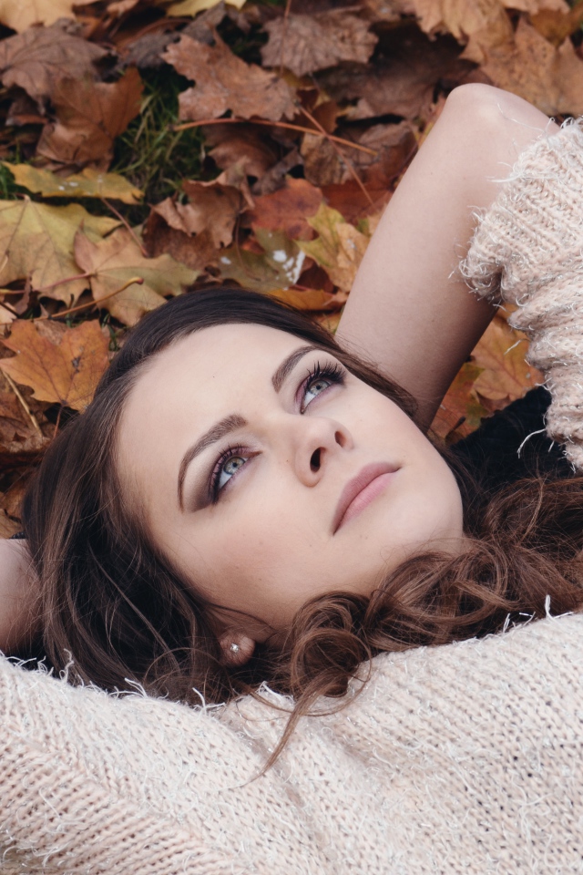 Красивая девушка в свитере лежит на опавших листьях 