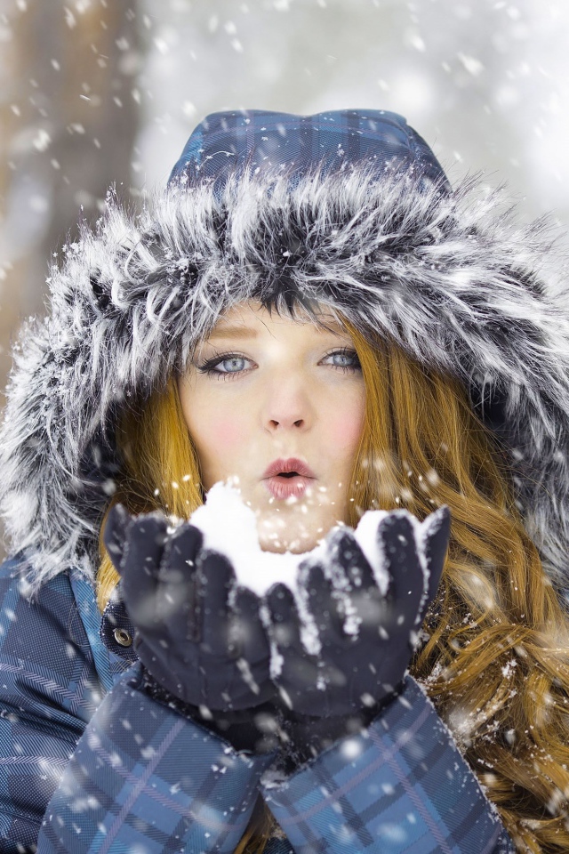 Красивая девушка в теплой куртке со снегом в руках