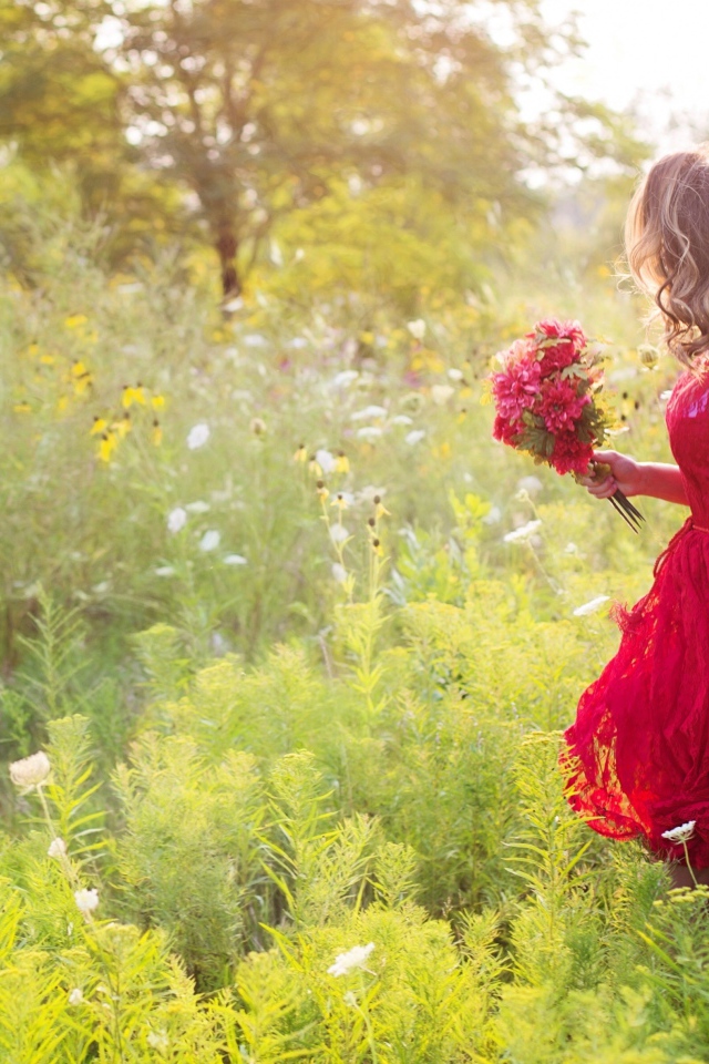 Красивая девушка в красном платье гуляет с букетом в руках по траве