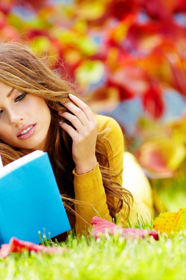 Красивая девушка читает книгу лежа на зеленой траве