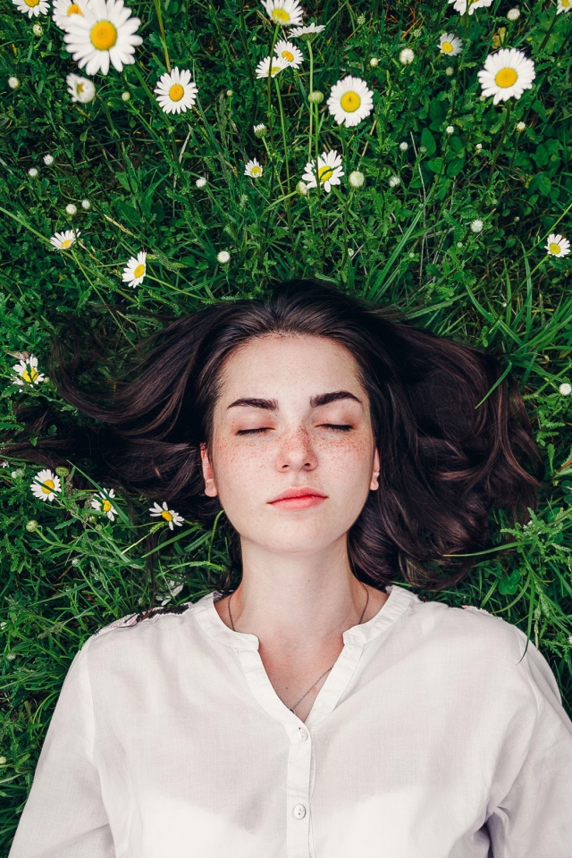 Красивая девушка лежит на зеленой траве с ромашками