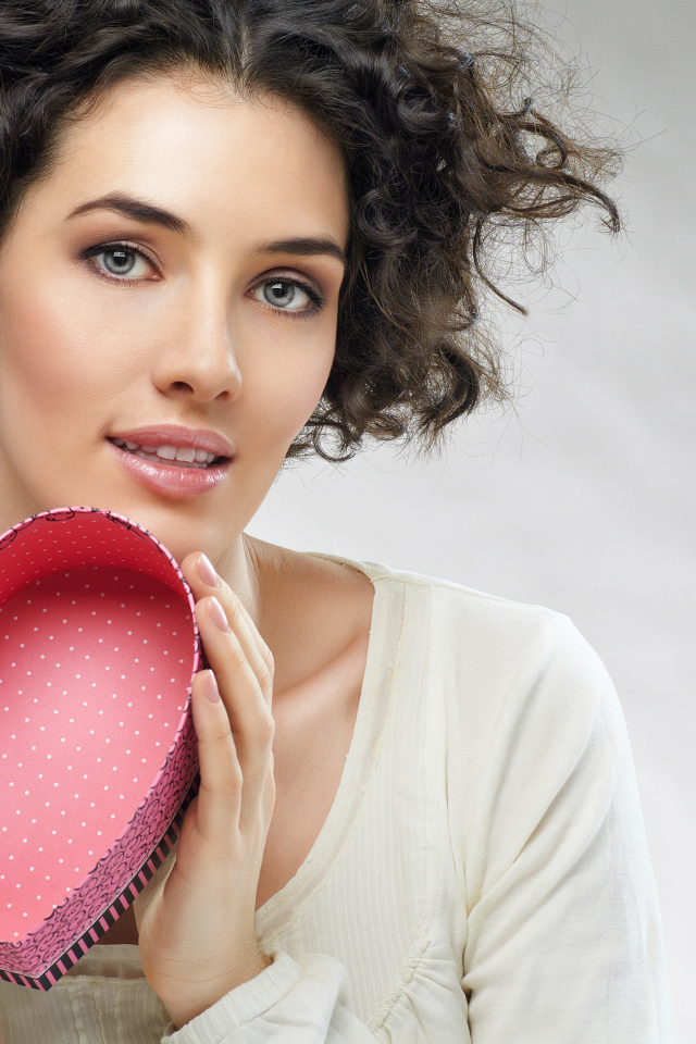 Красивая девушка с коробкой в форме сердца в руках на сером фоне