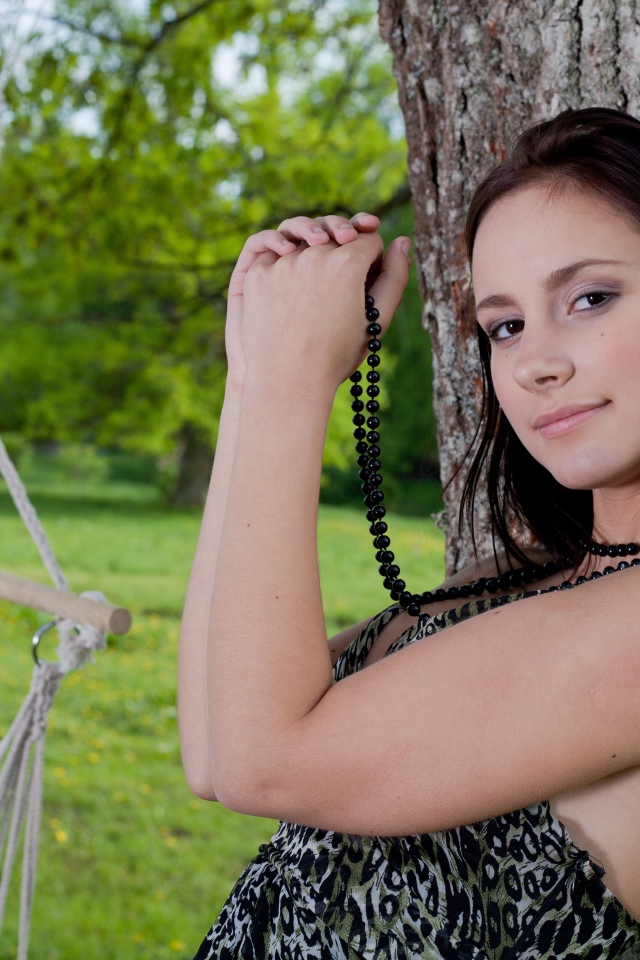 Красивая девушка с черными бусами под деревом