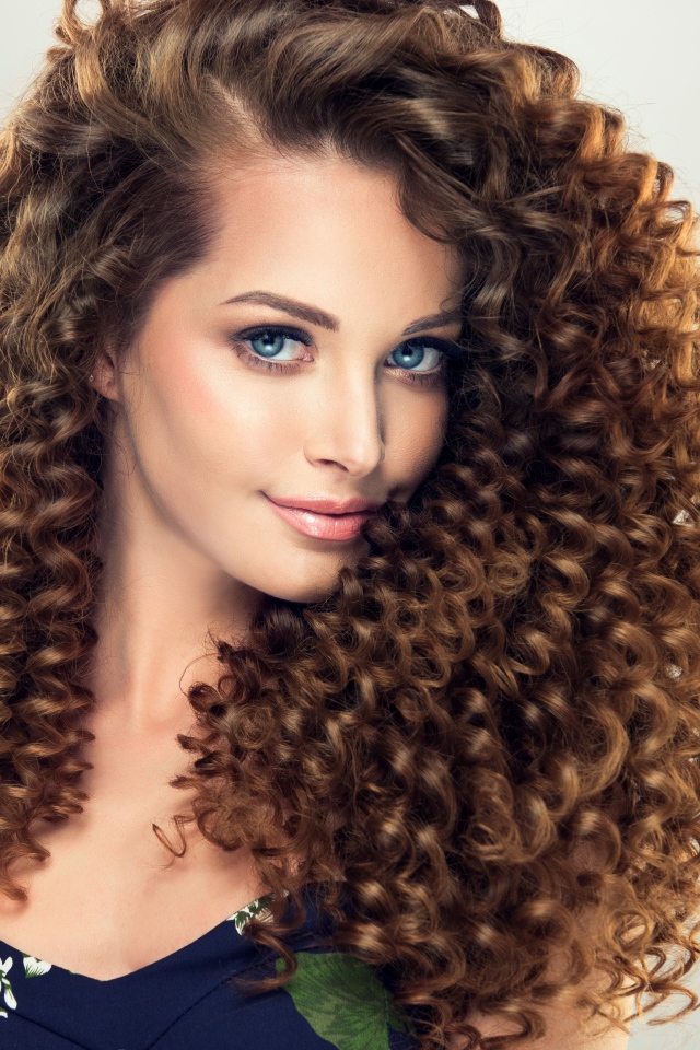 Красивая девушка с длинными волнистыми волосами на сером фоне