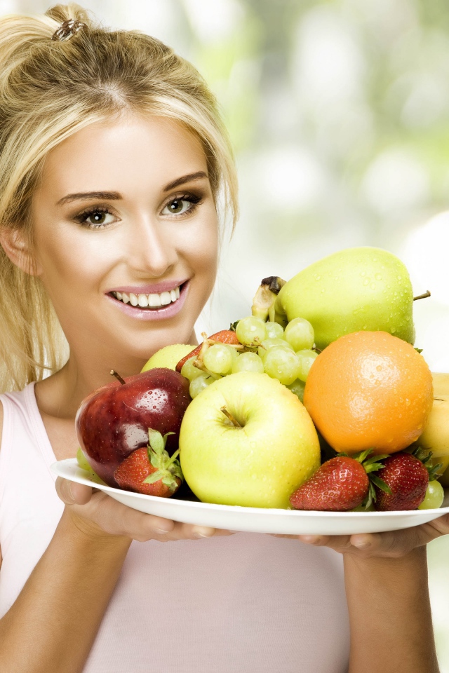 Красивая улыбающаяся блондинка с тарелкой с фруктами в руках