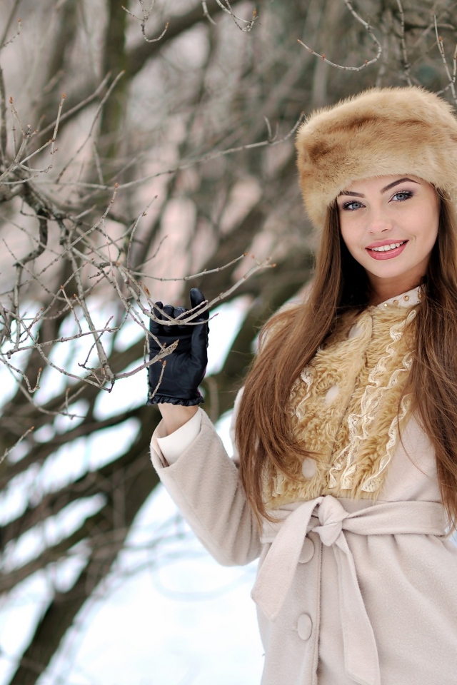 Красивая улыбающаяся девушка в шапке у дерева зимой