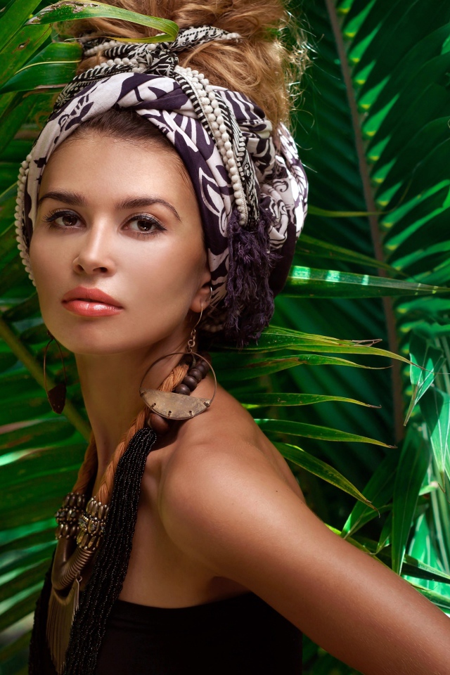 Красивая женщина в тюрбане с украшениями среди зеленых пальмовых листьев