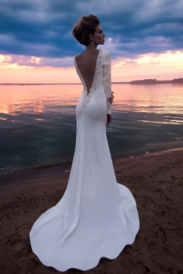 Красивая молодая девушка в свадебном платье у воды на закате 