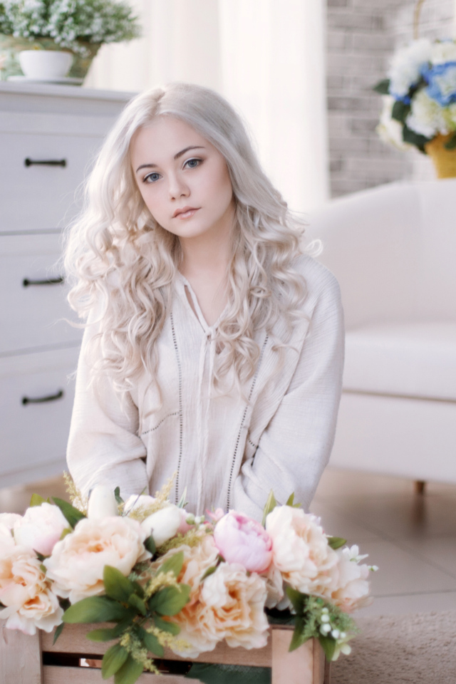 Девушка блондинка с пионами сидит в комнате