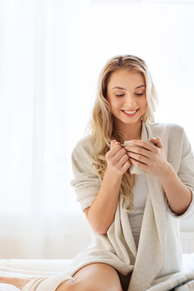 Нежная улыбающаяся девушка с чашкой кофе на кровати 