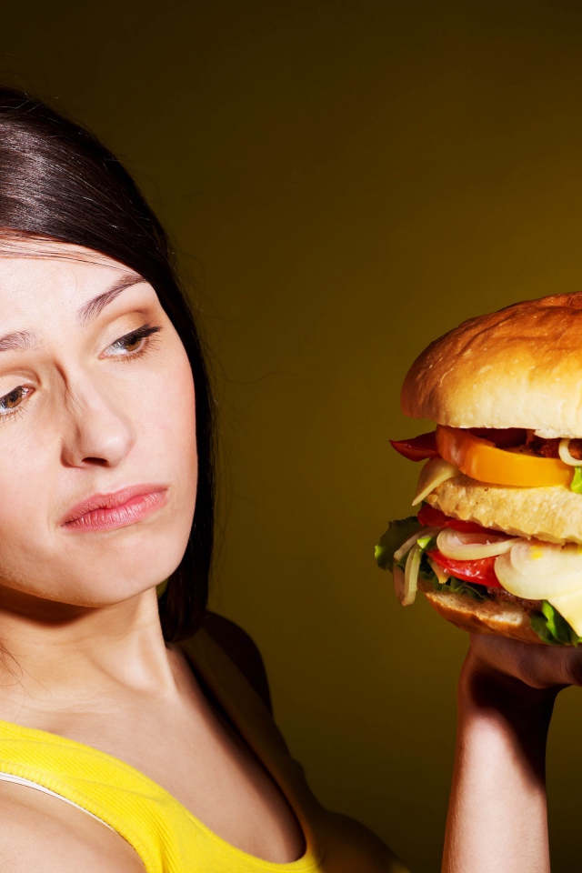 Недовольная девушка с большим гамбургером в руках 