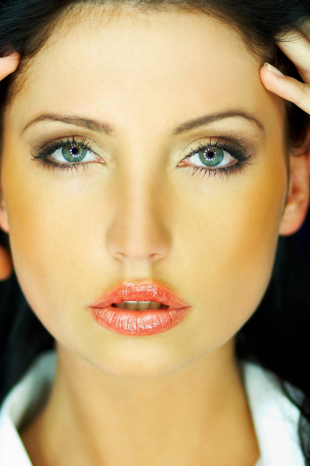 Зеленоглазая брюнетка держится руками за голову