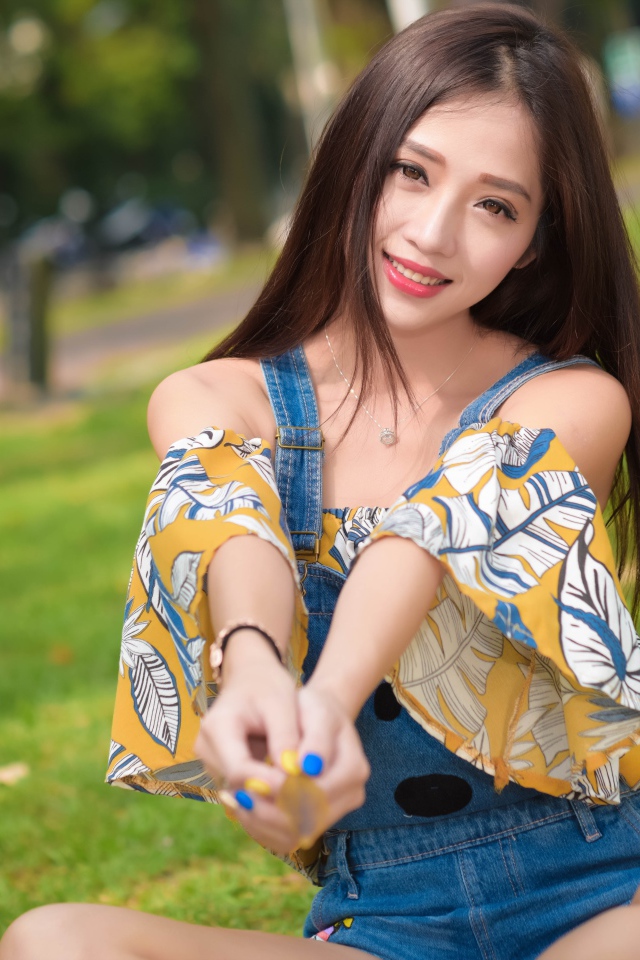 Улыбающаяся девушка азиатка сидит на траве